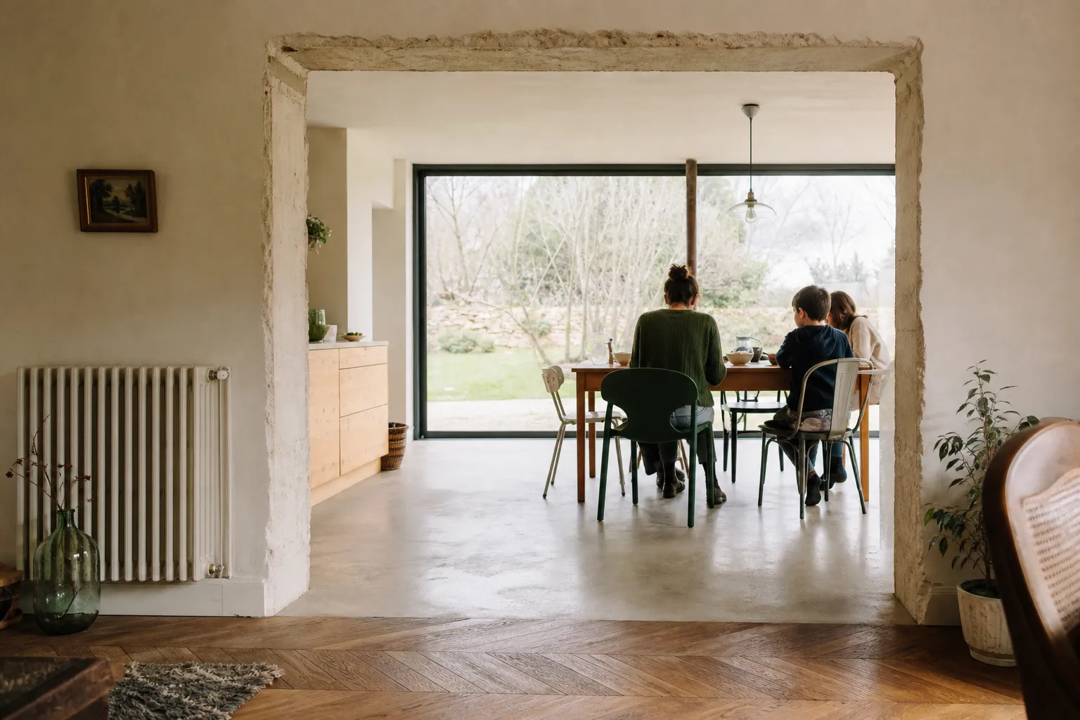 Vue depuis une pièce ancienne vers une extension neuve, parquet au premier plan, mur vitré au fond